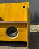 Close-up of the speaker chair's circular audio driver integrated into a warm-toned wooden panel. The combination of natural wood and precision speaker components highlights its sculptural contemporary design.