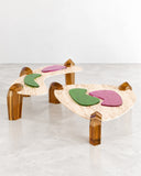 Islas sculptural floor table set featuring irregular pale tabletops, translucent amber-toned legs, and colorful organic inlays. The playful combination of materials, shapes, and colors creates a distinctive contemporary accent for curated interiors.