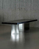 Modern dining table with a dark surface and metallic base against a textured wall. BLACK MOON | Modern Contemporary Table | Limited Edition