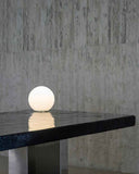 White spherical lamp on a dark marble table with a textured wall background. BLACK MOON | Modern Contemporary Table | Limited Edition