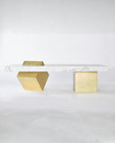 Arielle Assouline Coexist coffee table combining a veined marble surface with contrasting brass geometric supports. The sculptural design creates a distinctive focal point for sophisticated interiors.