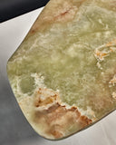 Close-up of the ONI coffee table's natural onyx top with distinctive translucent green and brown veining. The sculptural stone surface highlights its unique character and craftsmanship.