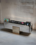 Sculptural media console crafted from reflective metal panels. A designer storage piece with a contemporary architectural silhouette.