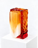 Adrian Cruz Porta Porta Stella Vase featuring an elongated vessel form with a luminous orange-to-cream finish, framed by an irregular red and amber sculptural surround. Its vivid colour transitions and textured detailing create a bold decorative statement for contemporary interiors.