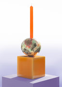 Decorative candle holder with a colorful sphere and an orange candle on a white background