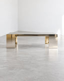 Contemporary Aura coffee table featuring a reflective metallic top and slim cylindrical metal legs. Its minimalist construction combines a refined finish with clean architectural proportions.