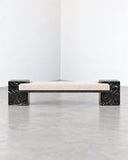 CoExist bench featuring a light upholstered or stone-toned rectangular seat between contrasting dark Nero stone end supports. The linear silhouette combines material contrast with minimalist contemporary design.