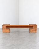 CoExist bench featuring an elongated orange travertine seat and matching substantial stone end supports. The warm mineral tones and natural surface texture create a sculptural contemporary seating piece.