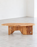 Sculptural Gia coffee table featuring a warm-toned natural wood top with an organic live-edge profile and chunky wooden supports. The solid timber construction highlights the natural grain and character of the wood.