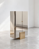 Sculptural X armoire featuring a tall, narrow cabinet form with reflective metallic panels and a contrasting geometric base. The vertical proportions and clean lines create a contemporary storage piece with an architectural presence.