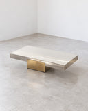 X coffee table featuring a low rectangular stone top with subtle natural veining and a geometric metallic pedestal base. The contrasting materials create a refined architectural centerpiece for contemporary interiors.
