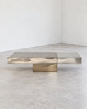 Contemporary X coffee table with a slim rectangular stone top and sculptural metallic supports. Its low profile and geometric construction emphasize clean lines and material contrast.