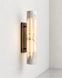 ETAMORPH Aura Sconce features a vertical cylindrical shade with luminous, veined stone and a dark wall-mounted fixture. Its warm illumination and understated sculptural form create an elegant accent for contemporary interiors.