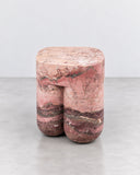 ETAMORPH Chunky Stool in Breccia Acquasanta features a compact, rounded rectangular seat supported by two substantial cylindrical legs. The pink and burgundy stone displays dramatic natural patterning, making each stool a distinctive sculptural accent.