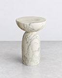 ETAMORPH Dome Side Table features a shallow, rounded tabletop and a sculptural pedestal base in white marble with expressive grey veining. Its elegant proportions and continuous stone form make it a refined accent for contemporary living spaces.