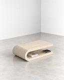 ETAMORPH Fold Coffee Table in travertine features a low, rounded profile with layered horizontal forms and a warm beige stone finish. Its folded, architectural silhouette combines understated natural texture with contemporary sculptural design.