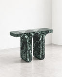 ETAMORPH Fold Console Table features a long, slim top with two substantial sculptural supports in deep green stone with contrasting white veining. Its architectural proportions and rich natural pattern bring a bold material statement to contemporary entryways and living spaces.