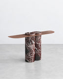 ETAMORPH Jumbo Console features a slim, elongated tabletop supported by a substantial cylindrical pedestal in burgundy marble with expressive white veining. Its contrasting proportions and sculptural stone base create a refined architectural accent.