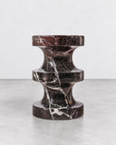 ETAMORPH Spira Side Table in Rosso Levanto features a sculptural hourglass-like profile carved from deep burgundy marble with striking white veining. Its rhythmic curves and rich natural pattern bring a refined, architectural presence to contemporary spaces.