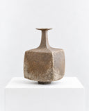 Genaro Hoepfner RNE03 Vessel featuring a compact, rounded body with a narrow elongated neck and a richly textured earthy brown surface. Its sculptural proportions and weathered finish give this decorative vessel a distinctive organic character.