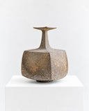 Genaro Hoepfner RNE04 Vessel featuring a broad, asymmetrical body, a slender tapered neck, and a textured brown surface with natural-looking tonal variation. Its irregular silhouette and tactile finish create a distinctive sculptural object for contemporary interiors.