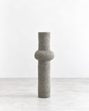 Genaro Hoepfner RO06 Ceramic Object featuring a tall cylindrical form with a rounded raised band around its centre and a coarse grey textured finish. Its minimal geometric silhouette and tactile surface make it a striking contemporary decorative object.