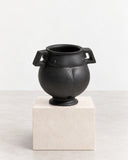 IAMMI Champion Size S features a rounded black vessel form with a short neck and bold geometric side handles. Its dark, glossy finish and compact sculptural silhouette create a striking decorative accent.