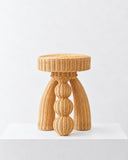 Pupa side table featuring a cylindrical woven fiber top and a sculptural central base formed from rounded stacked elements. The warm natural texture and organic geometry create a distinctive contemporary accent table.