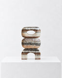 LS-03 brown marble sculpture composed of stacked rounded forms with a central opening and compact arched base. The layered brown and cream stone veining gives this sculptural object a distinctive natural pattern.