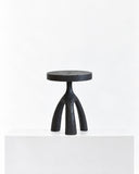 Tecolli wood sculpture featuring an abstract figure with a circular central detail, curved upper element, and slender tripod-like base. Its dark sculptural finish combines minimalist geometry with an expressive collectible form.