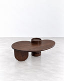 METAMO Axis Coffee Table featuring an elongated oval dark wood top with a raised circular detail and chunky cylindrical supports. Its low sculptural profile, rich wood grain, and minimalist geometry create a distinctive contemporary centrepiece.