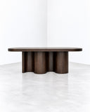 METAMO Kairo Bench featuring an elongated oval tabletop in dark stained wood, supported by a sculptural base of rounded, fluted wooden forms. Its rich wood grain and architectural silhouette create a distinctive contemporary statement for luxury residential and hospitality interiors.