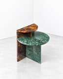 Noemi Saga Café Marble Side Table featuring overlapping circular green stone surfaces with natural veining and a contrasting upright slab in warm brown and amber tones. Its asymmetrical composition and sculptural silhouette make it a distinctive accent for contemporary interiors.
