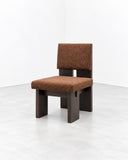 Noemi Saga Hawaii Dining Chair featuring a structured dark wooden frame, a straight upright backrest, and a seat upholstered in textured rust-brown fabric. Its strong geometric lines and warm upholstery bring understated character to contemporary dining spaces.
