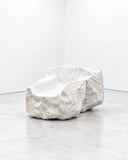 Noemi Saga Iceberg Armchair featuring a low, sculptural silhouette with irregular, rock-like contours and a pale textured surface. Its bold organic form blurs the boundary between functional seating and contemporary collectible design.