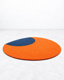 Noemi Saga Moon Art Rug featuring a bold circular orange field accented by an asymmetrical dark blue shape. Its minimalist colour blocking and graphic composition introduce a playful contemporary statement to living spaces.
