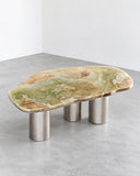 Organic Oni coffee table featuring an irregular natural stone top with expressive green and amber veining, supported by cylindrical metallic legs. The contrast between the patterned stone and polished metal creates a distinctive contemporary centerpiece.