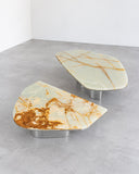Oni nesting coffee tables featuring irregular natural stone tops with distinctive green and amber veining. The two sculptural tables offer flexible arrangements with contrasting organic shapes and polished metallic supports.