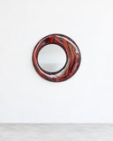 Onno Adriaanse Magma Mirror featuring a circular reflective centre surrounded by a richly patterned red, burgundy, and dark-toned frame. Its fluid, marbled detailing creates a bold contemporary statement for residential and hospitality interiors.