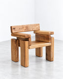 Onno Adriaanse Timber Armchair in Elm featuring a substantial wooden frame with squared arms, a solid seat, and visible natural grain in warm honey-brown tones. Its robust proportions and minimalist geometry highlight the character of the wood.