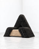 Richard Yasmine Furrybum Black Fur Armchair featuring a dramatic triangular silhouette covered in long black fur, with a contrasting tan upholstered seat. Its tactile finish and unconventional sculptural form make it a bold statement piece.