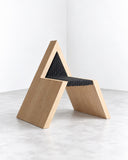 Richard Yasmine Woven Whispers Chair featuring an angular, triangular wooden frame with a dark woven seat and backrest. Its architectural geometry and contrast between natural wood and woven texture create a distinctive contemporary seating piece.