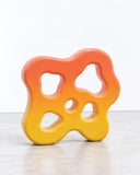 Ryan Mercer Blob Shelf Jr featuring an irregular, rounded frame in a vibrant orange-to-yellow finish with multiple organic openings. Its fluid silhouette combines playful sculptural design with functional wall storage.