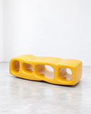 Ryan Mercer Block Credenza featuring a bright yellow, elongated form with rounded edges and a series of sculptural open compartments. Its bold colour and playful geometric design make it a distinctive contemporary storage piece.