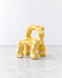 Ryan Mercer Butter Chair featuring a sculptural yellow frame composed of rounded, interconnected forms with circular cutouts. Its playful geometry and distinctive silhouette reinterpret contemporary seating as functional design art.