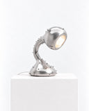 Ryan Mercer Not So Big Lamp featuring an articulated, sculptural metal frame with a rounded reflective shade and polished silver finish. Its mechanical detailing and compact silhouette combine functional lighting with contemporary industrial character.