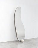 1931 wall mirror featuring a tall, slender reflective surface with an elongated organic outline and slim metallic edging. Its fluid vertical silhouette creates a sculptural contemporary mirror.