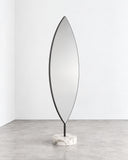 Aglaia floor mirror featuring a tall, narrow reflective panel with a pointed oval silhouette and slim metallic edging. The elongated sculptural form creates a refined contemporary full-length mirror.