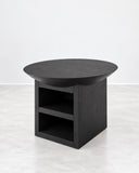 Atlante side table featuring a dark rounded tabletop and a solid central pedestal with an open rectangular storage compartment. Its bold proportions combine functional storage with minimalist contemporary design.