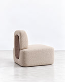 SECOLO Clip Lounge Chair featuring softly textured cream upholstery and a distinctive contrasting brown inset along the curved backrest. Its compact, sculptural silhouette combines tactile detailing with a relaxed contemporary form.